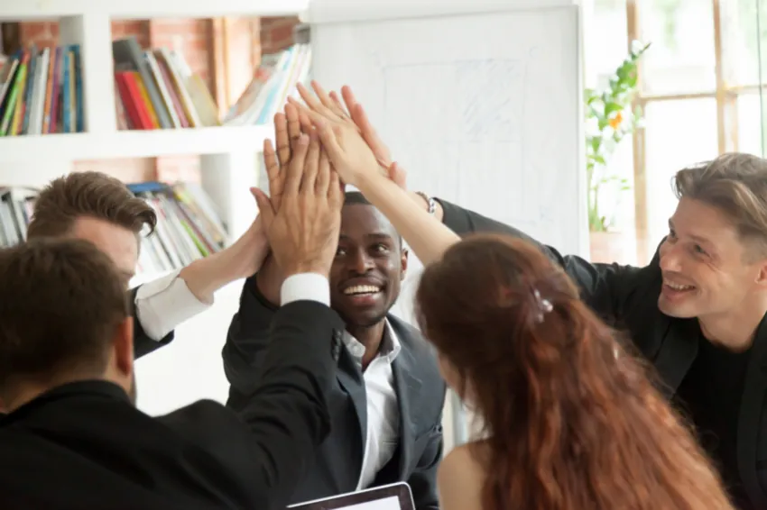 Company intranet: four male employees and a female employee sitting around a round table are putting hands together