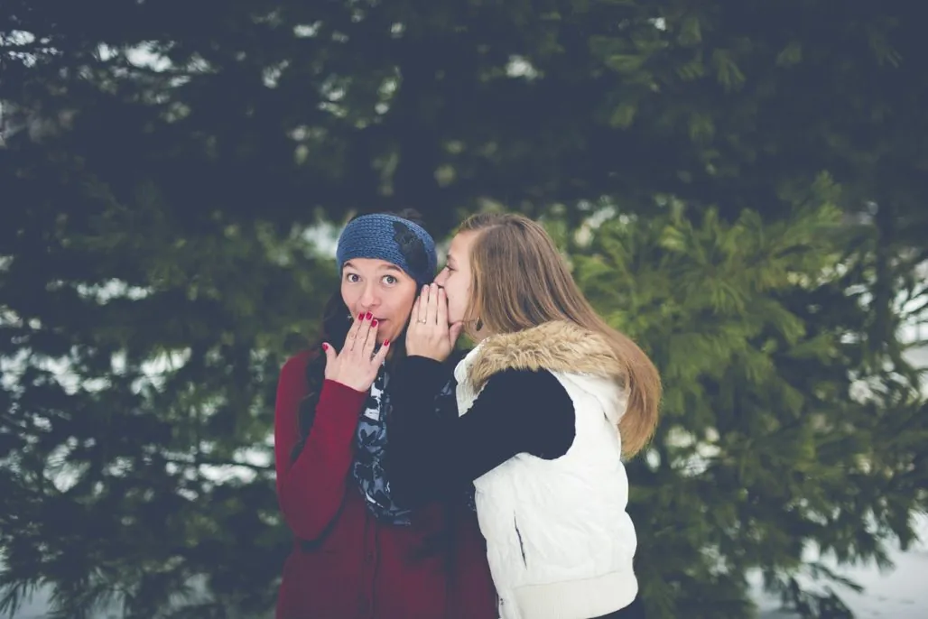 Communication mistakes - woman whispering into her friend's ear