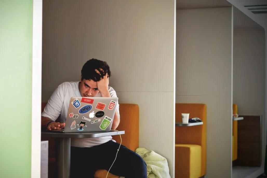 Company culture - man working in cubicle, looking at laptop with stressed look on his face