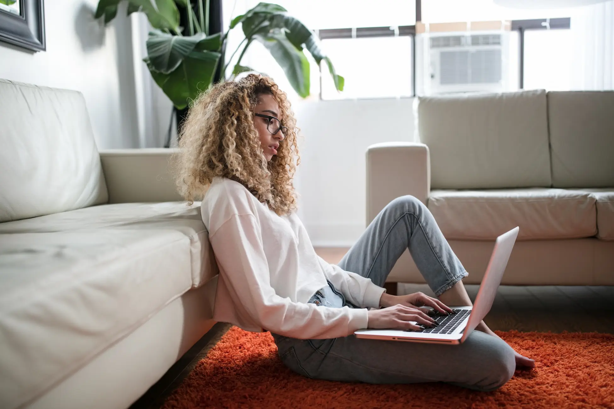 Woman working from home on laptop sitting against couch