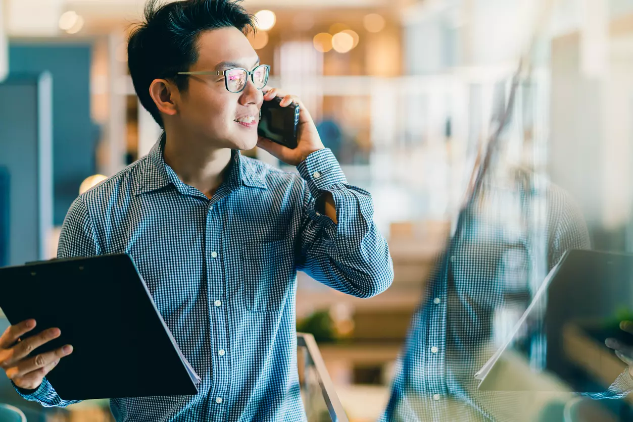 Employee communication app benefits: a man in a striped blue shirt is talking on his smartphone.