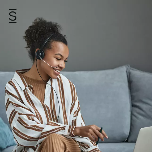 Customer-First Culture - woman wearing headset sitting on grey sofa using laptop