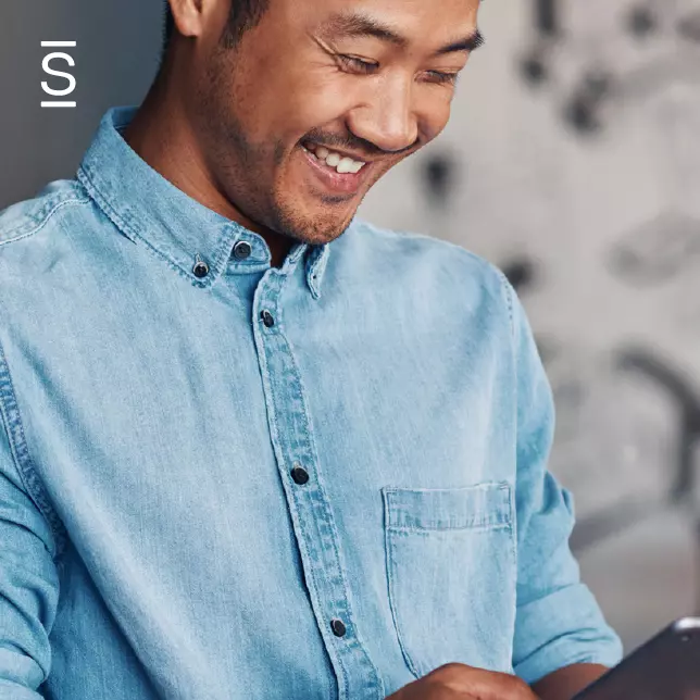 Employee engagement - man in denim shirt smiling and looking at smartphone