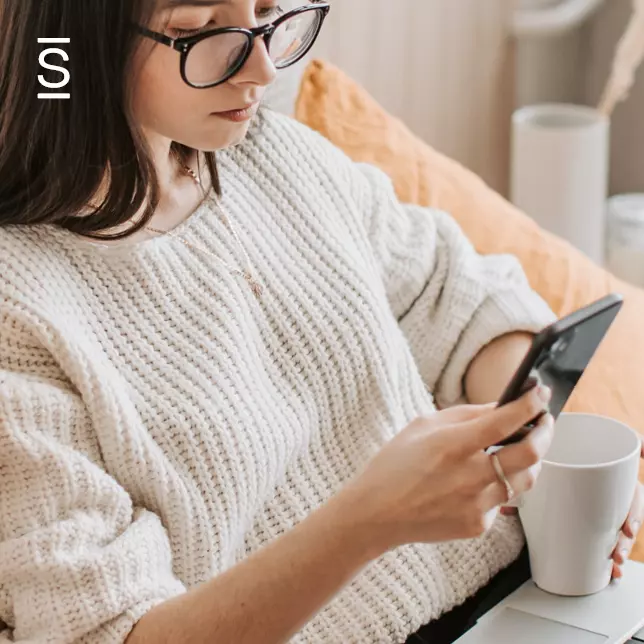 Employee communication app - woman with glasses holding coffee mug and using smartphone