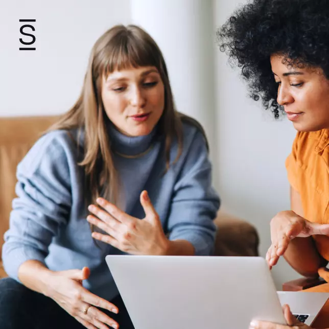 Employee experience - two female employees having a discussion while looking at laptop screen