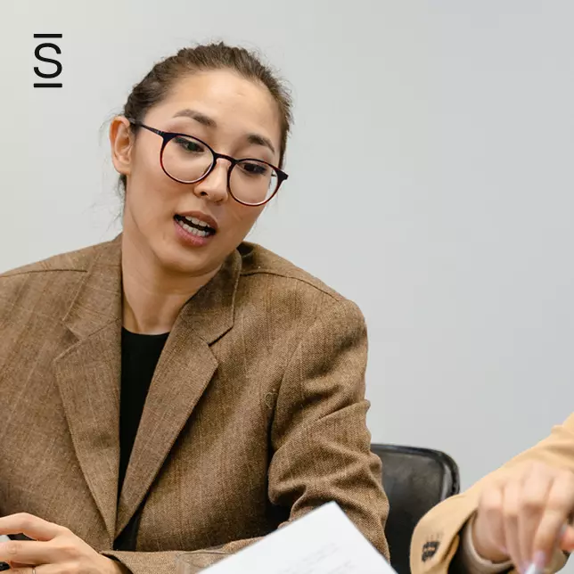 Characteristics of a good leader - woman in glasses and a blazer speaking to unseen colleague