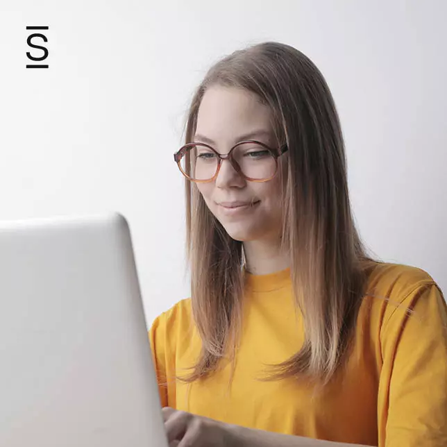 Employee engagement - woman with glasses and wearing yellow shirt using laptop computer