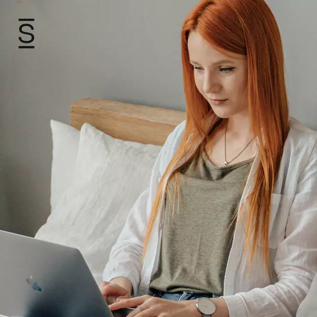 Working From Home - woman with red hair sitting on sofa and working on laptop