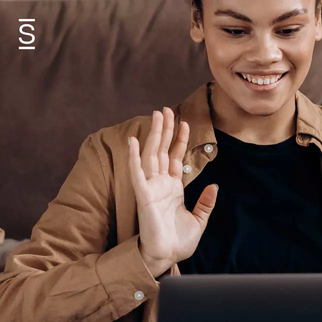 Remote Team Building - woman smiling and waving in virtual meeting on laptop