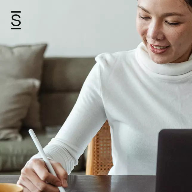 Work From Home - woman writing on unseen notepad while computer sits in front of her