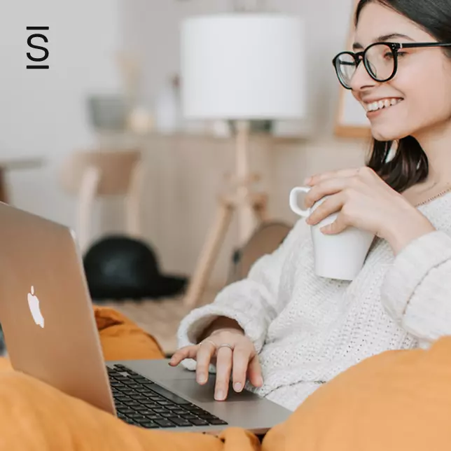 Employee Recognition - woman with glasses smiling while working on laptop and holding coffee mug