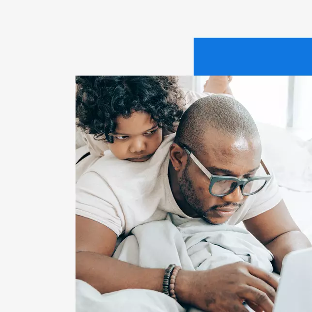 man with glasses working on computer while child sits on him