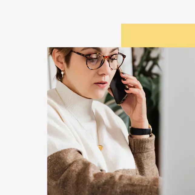 Company culture - woman with glasses speaking on smartphone and looking at computer screen