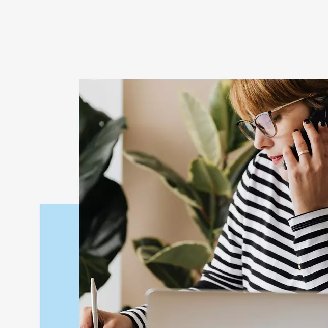 woman in striped shirt wearing glasses speaking on smartphone and writing notes down