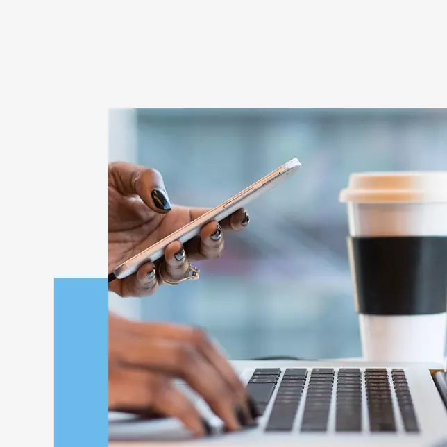 Employee experience - woman holding smartphone and using laptop while coffee cup sits in the background