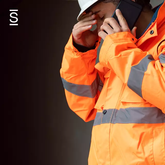 Deskless workers - man wearing hard hat and bright orange safety jacket and talking on cell phone