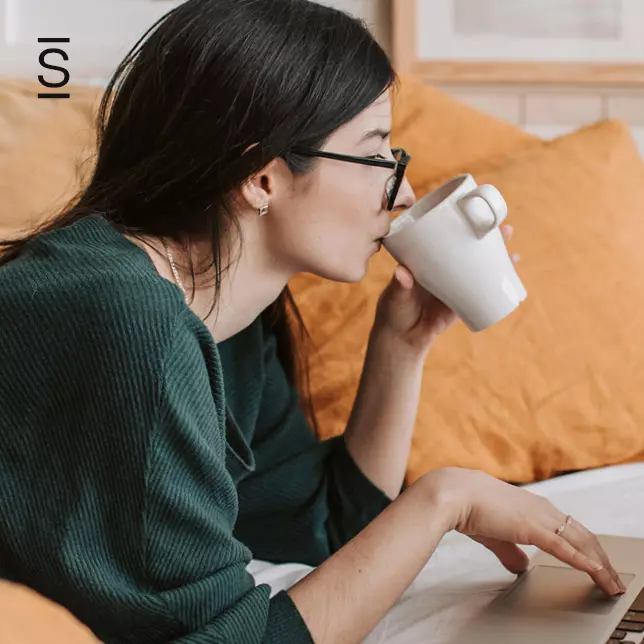 communication with remote workers - woman with glasses sipping from coffee mug and working on laptop computer