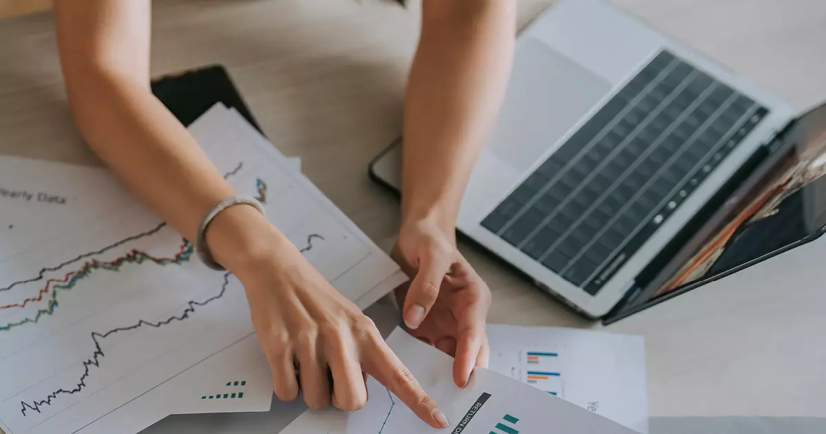 Internal Communications - employee working on laptop computer referring to papers with graphs on them