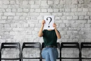 Diversity and inclusion - young woman candidate hiding face behind sheet with question mark