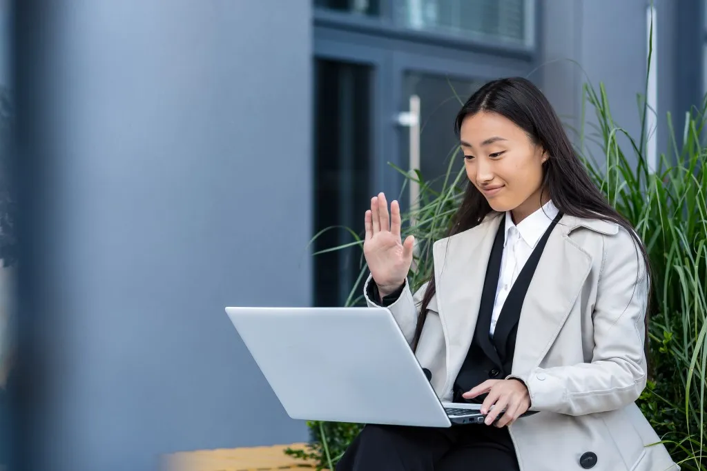 Build or buy intranet - Asian woman sitting on a bench near a modern building, checking intranet options