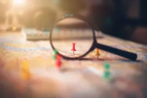 Employee experience: a magnifying glass focusing on a red board pin placed on a map