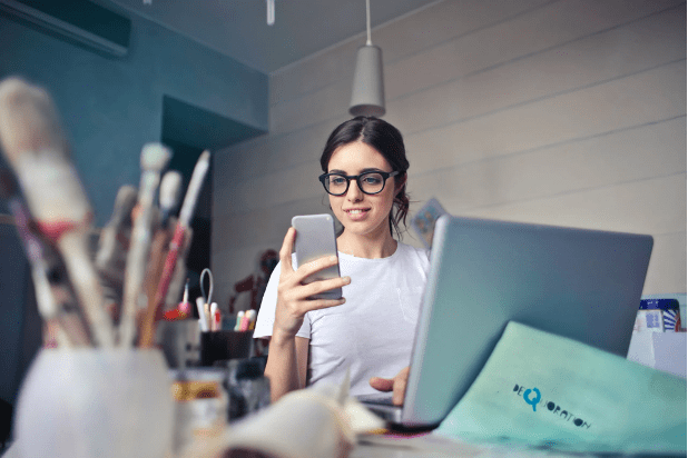 User Interface - woman in glasses looking at smartphone while sitting in front of laptop computer