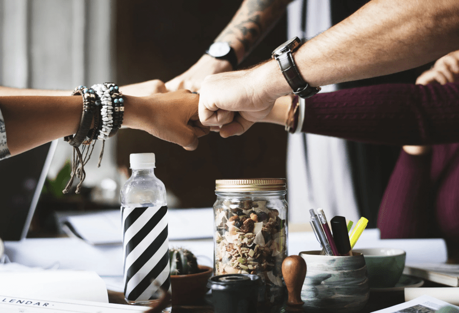 Brand reputation - group of employees doing a teamwork salute over a table